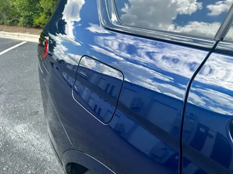 Blue car rear quarter panel with fuel door and sky reflections, parked outdoors
