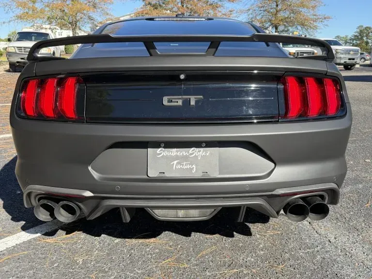 Rear view of a gray Ford Mustang GT with quad exhaust and red taillights in a parking lot