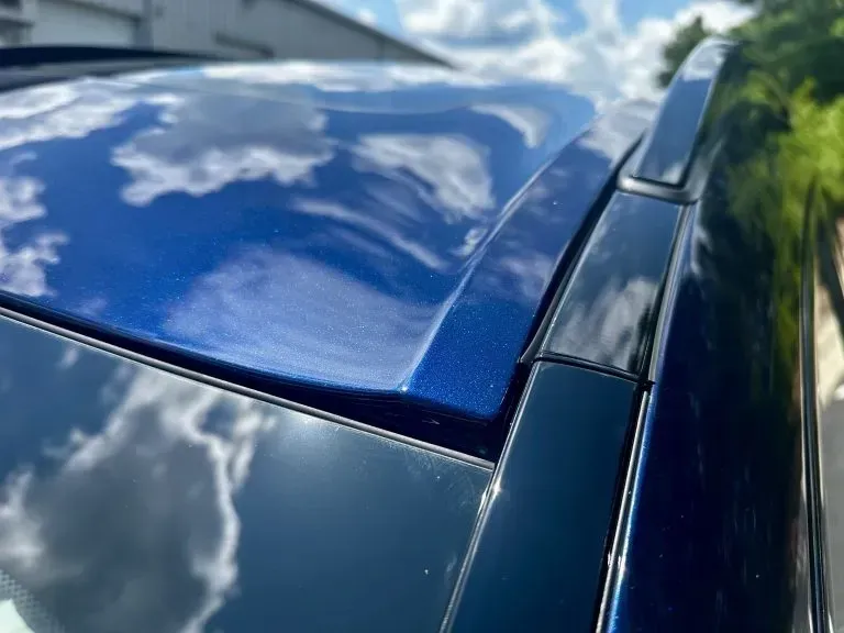 Close-up of a blue car roof and rear window reflecting clouds in the sky