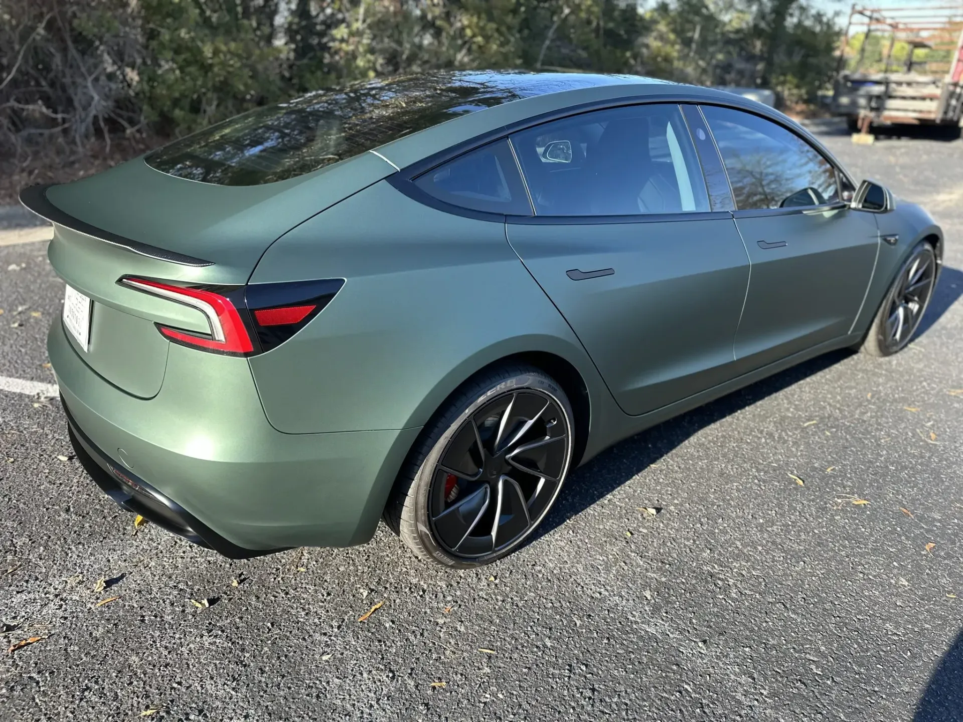 Matte green sporty sedan parked on a sunny roadside, viewed from the rear side.