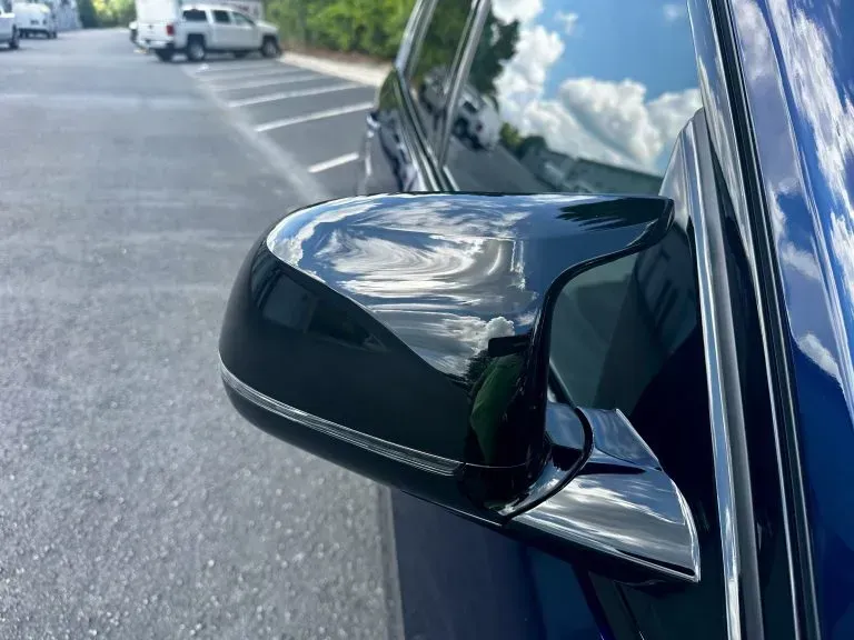 Black car side mirror with a visible crack on a street, parked beside the curb