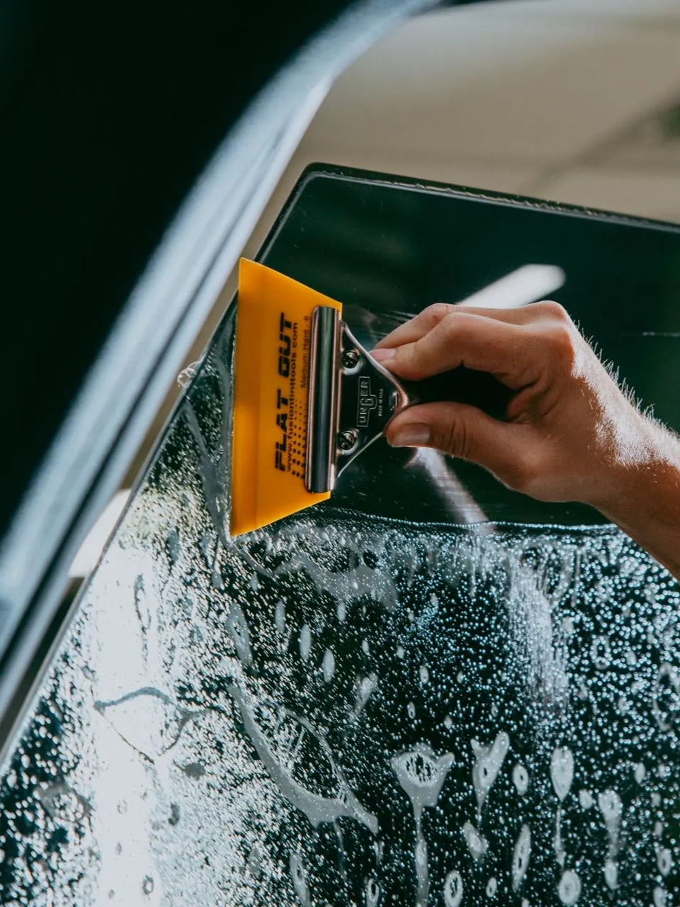 Hand scraping frosted car window with a yellow ice scraper, removing ice from glass