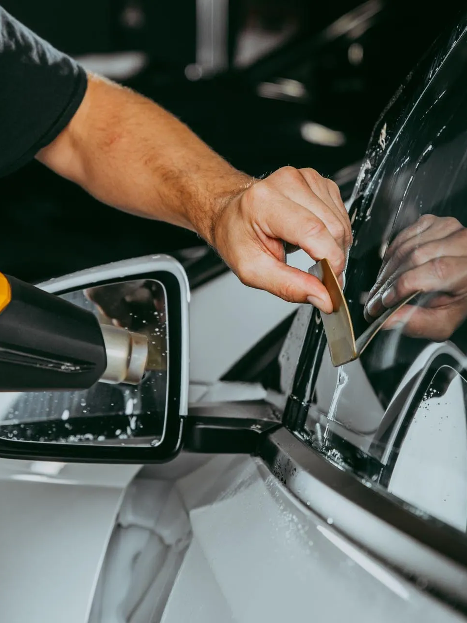 Person cleaning a car windshield with a squeegee beside the side mirror