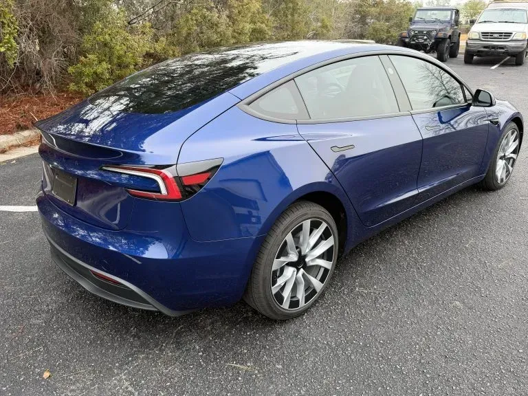 Blue Tesla Model Y parked on a wet street, rear three-quarter view
