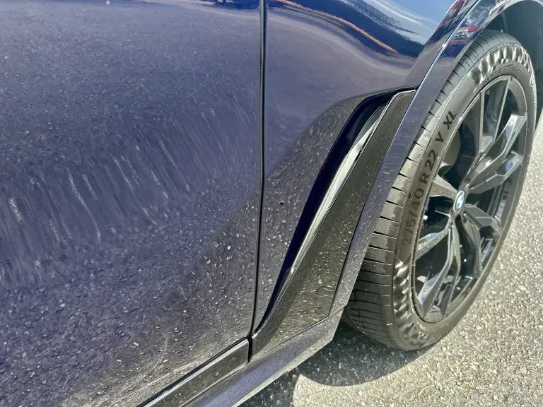 Close-up of a dark blue car’s rear wheel and side panel with dusty bodywork and a black rim.
