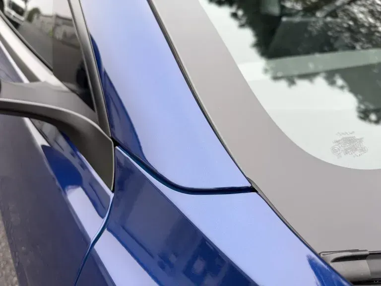 Blue car’s side panel with a visible dent and crease near the window edge