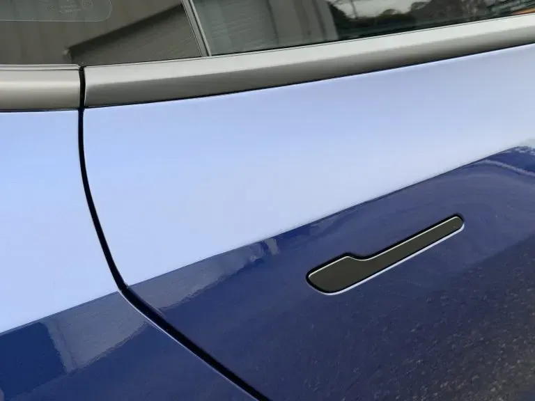 Close-up of a blue car door with a flush black handle and silver trim