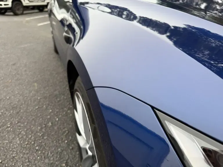 Close-up of a blue car’s front fender and headlight in a parking lot