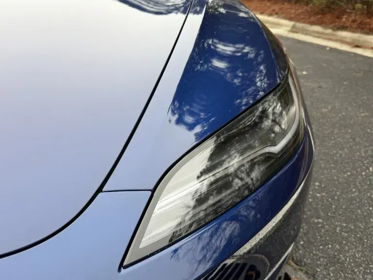 Close-up of a blue car’s front headlight and hood on a street