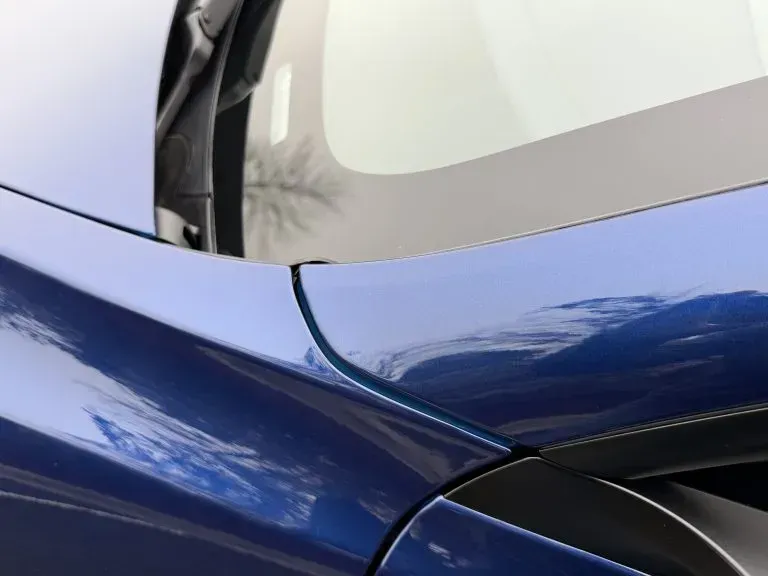 Close-up of a blue car’s rear quarter panel and window seam with visible body damage