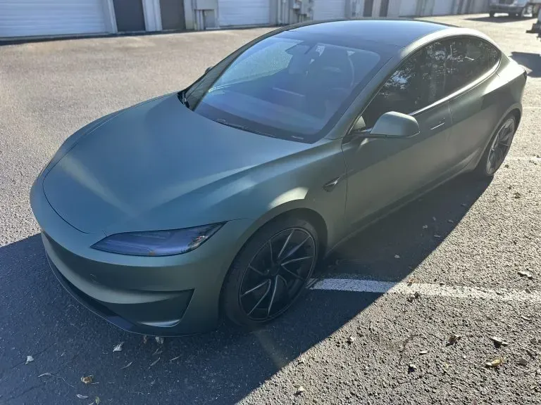 Gray Tesla parked in a sunlit lot, viewed from the front-left side.