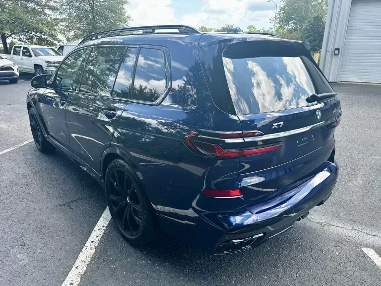 Dark blue BMW X7 SUV parked in a lot, rear three-quarter view.