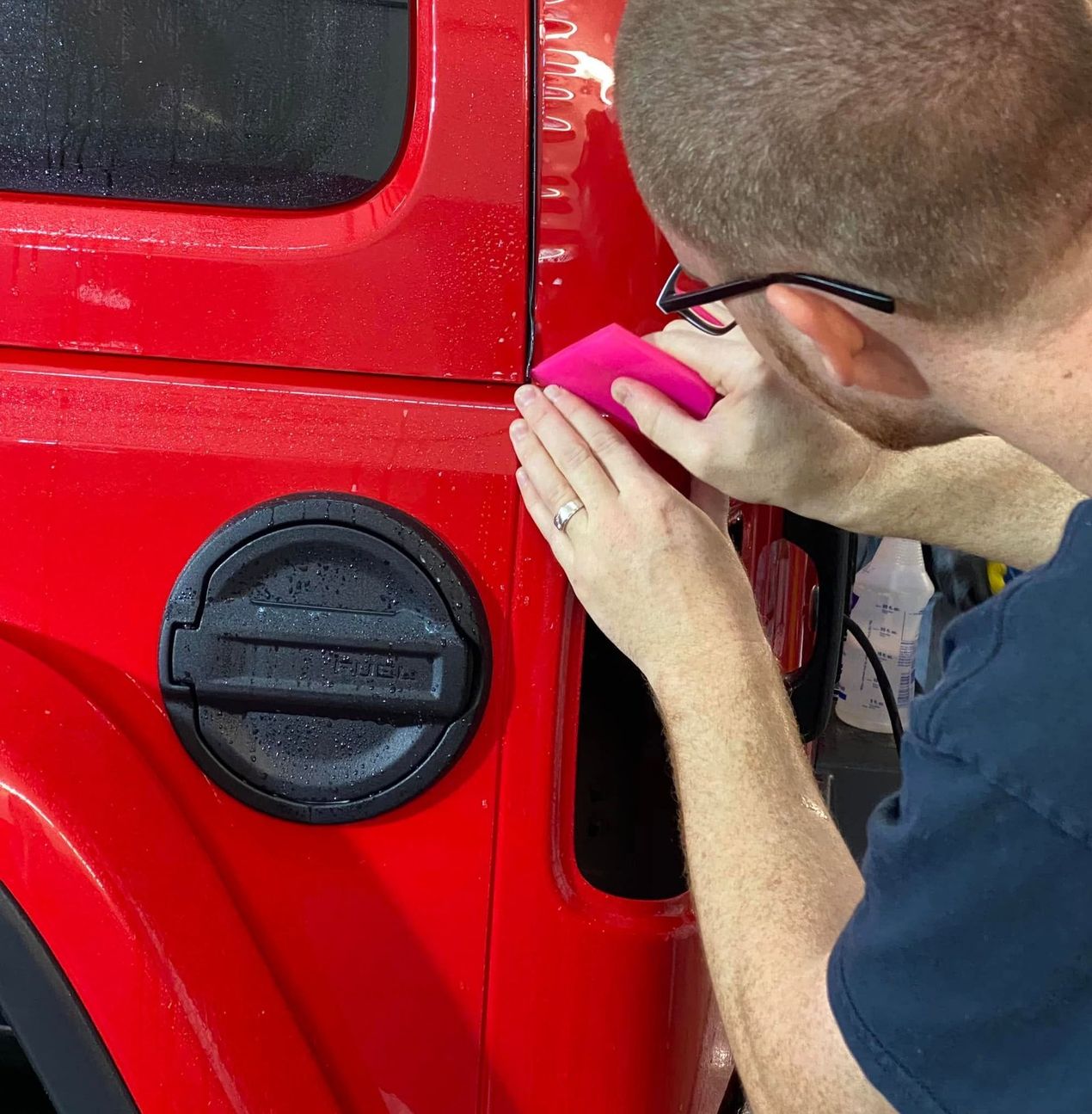Person polishing a red car door with a pink cloth near the fuel cap