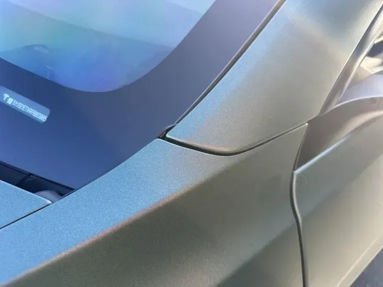 Close-up of a silver car's front corner and windshield in sunlight