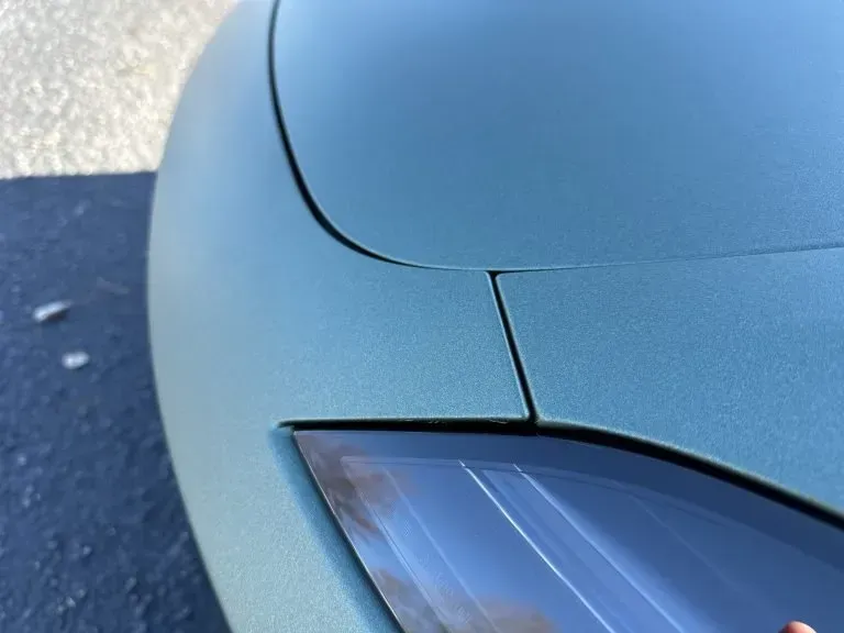 Close-up of a light blue car’s front corner and headlight on pavement