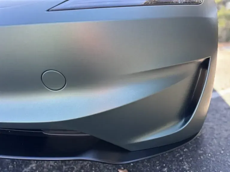 Close-up of a silver car’s front bumper with a circular sensor and black lower grille trim