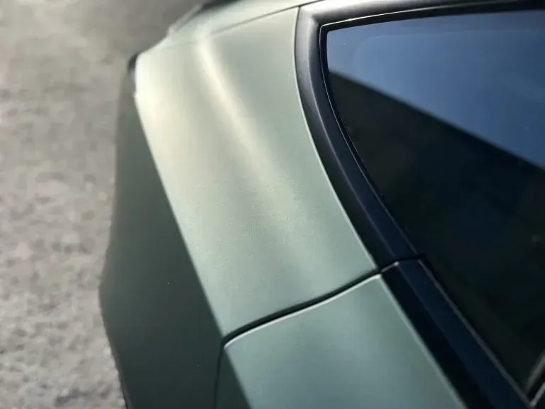 Close-up of a light green car rear panel and tinted window against pavement