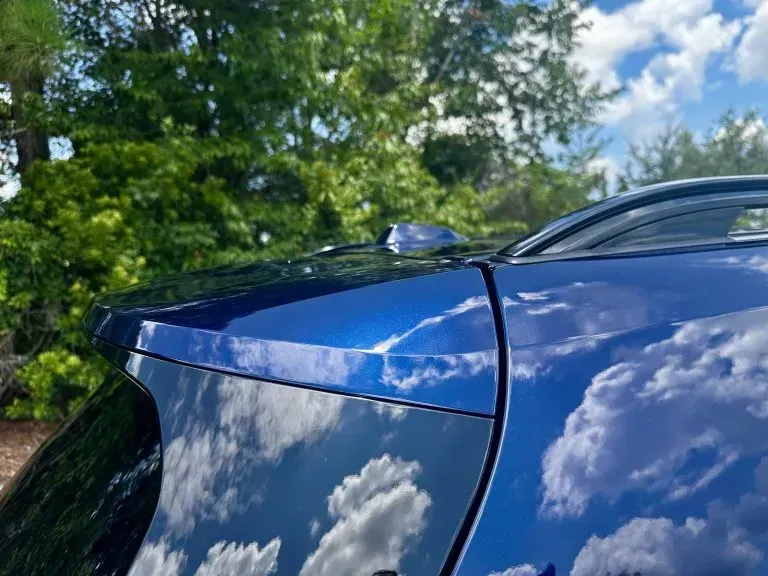 Blue car roof and windshield reflecting clouds under a partly cloudy sky.