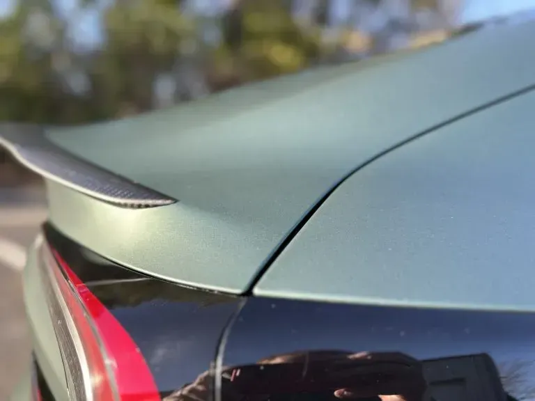 Close-up of a green car’s rear corner with a black spoiler and red taillight.