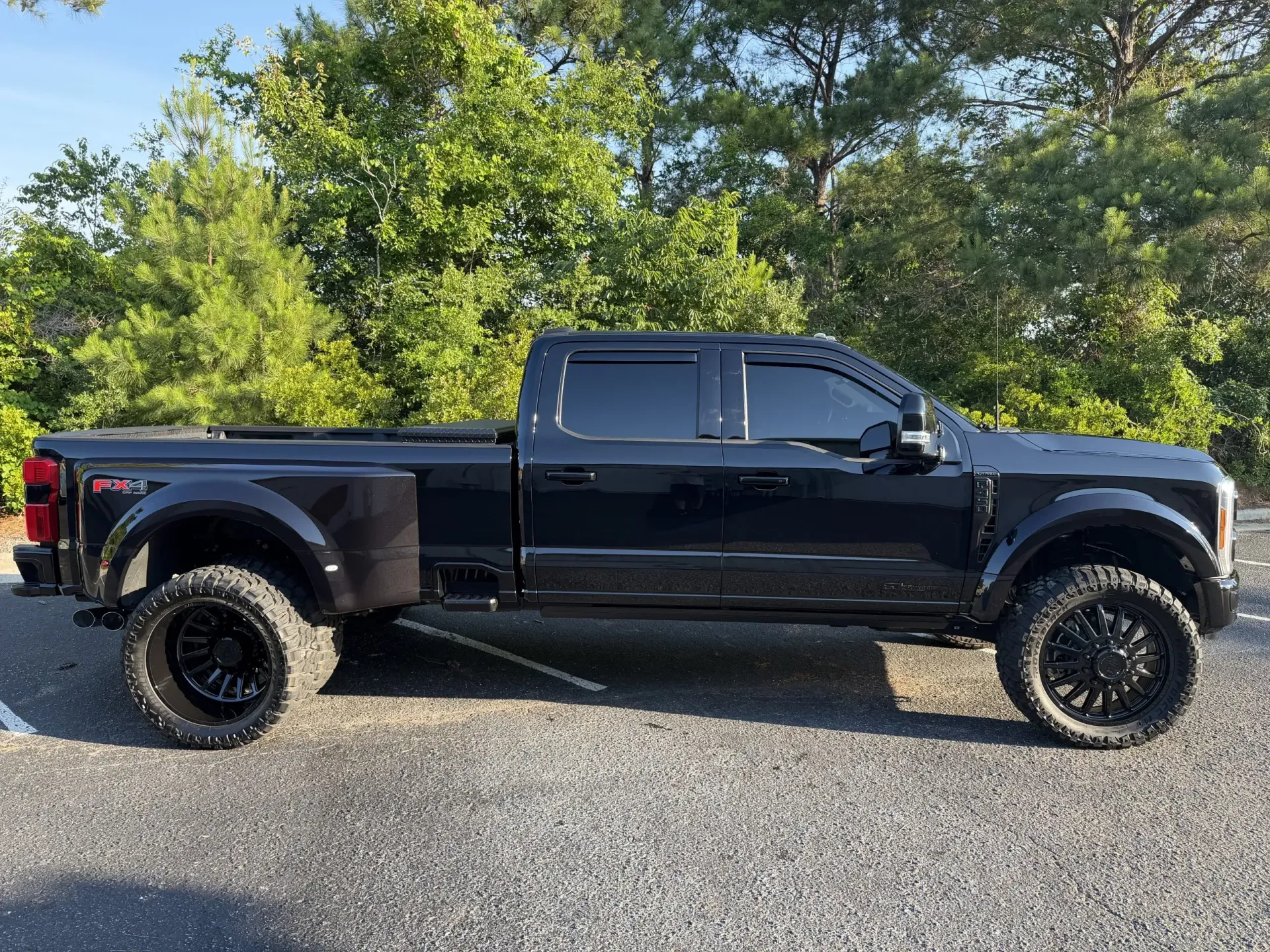 Black pickup truck with lifted suspension parked on gravel in front of trees