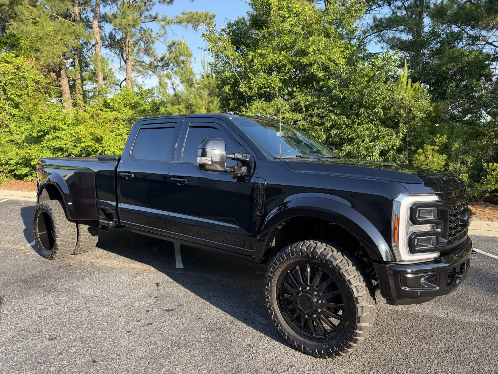 Black lifted pickup truck parked on gravel with trees in the background