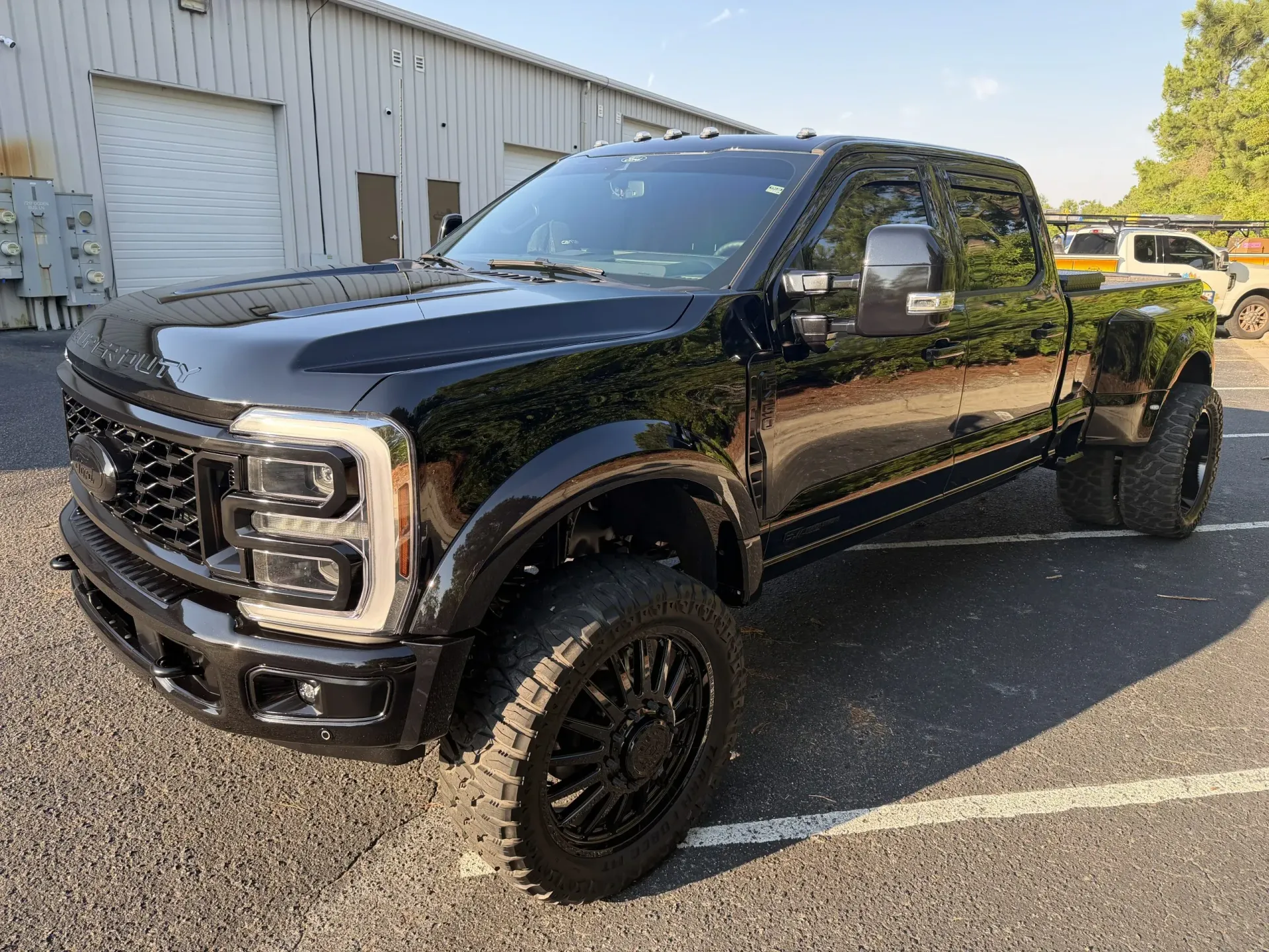 Black lifted pickup truck parked outside an industrial building on a sunny day