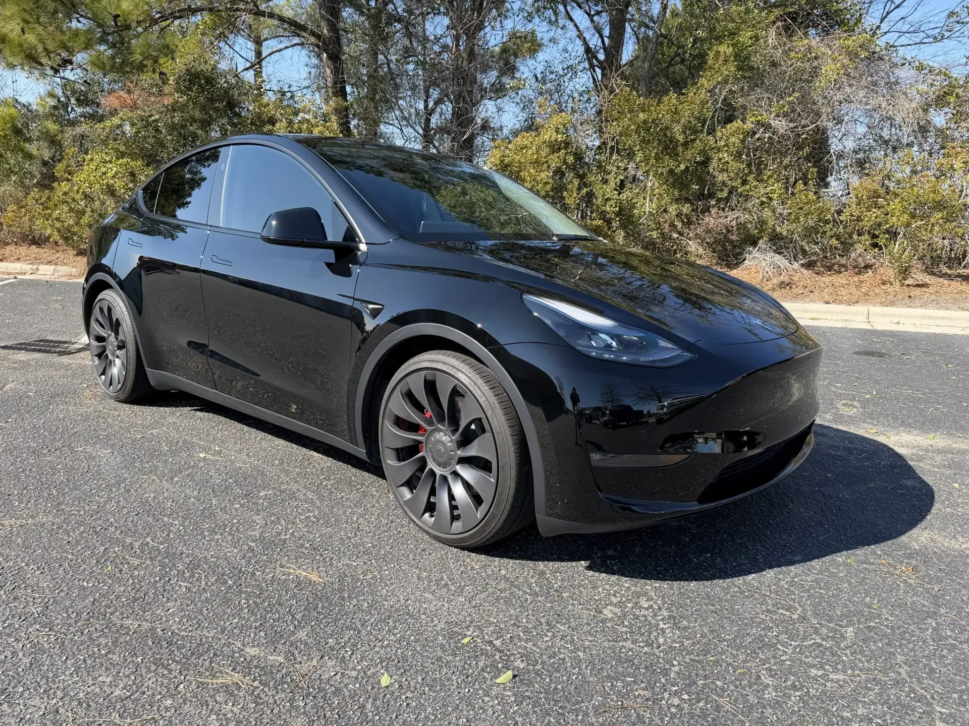 Black Tesla sedan parked on gravel with trees in the background