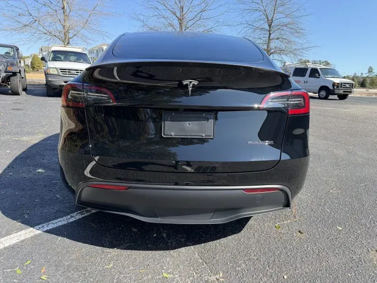 Rear view of a black Tesla Model Y parked in an outdoor lot on a sunny day