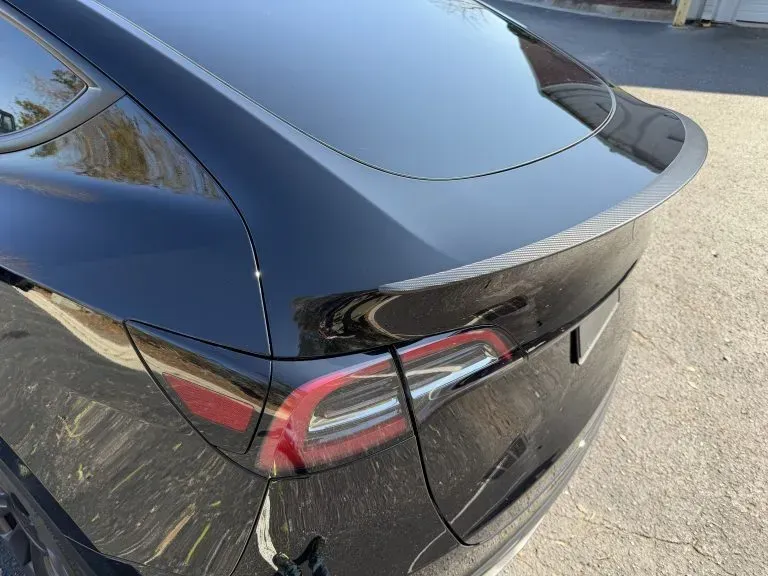 Rear of a black Tesla sedan with a damaged rear bumper and cracked taillight on a road