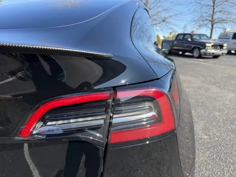 Close-up of a black Tesla’s rear taillight and trunk on a sunny parking lot.