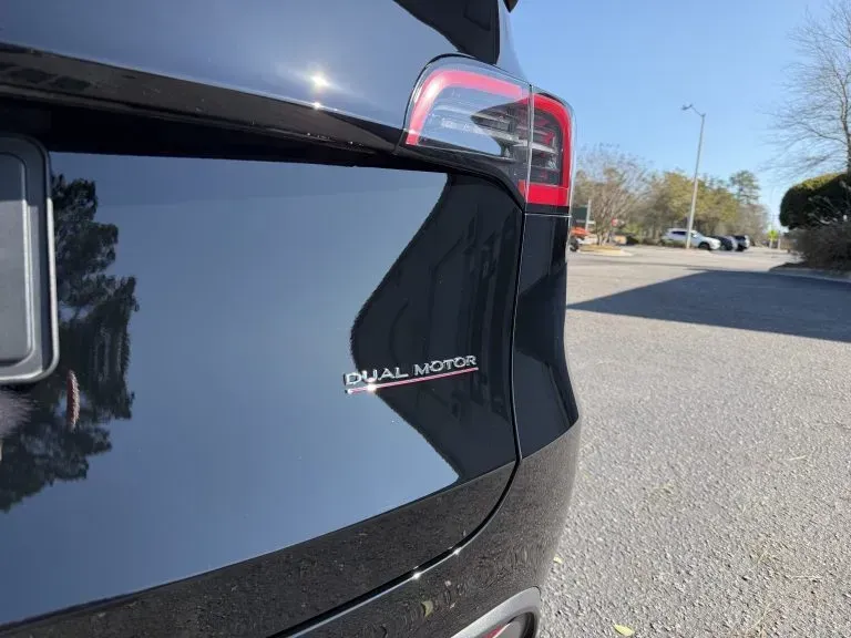 Close-up of a black car’s rear corner and taillight on a sunny street.