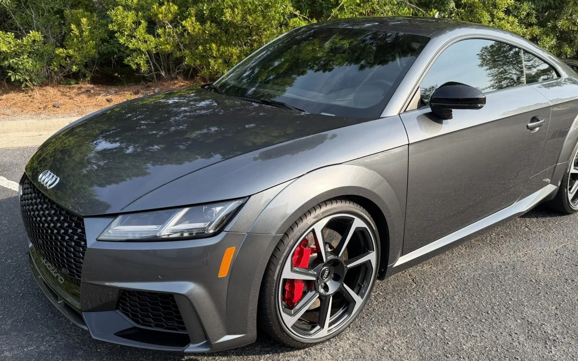 Gray sporty sedan parked outdoors, front-left view, with red brake calipers and dark alloy wheels