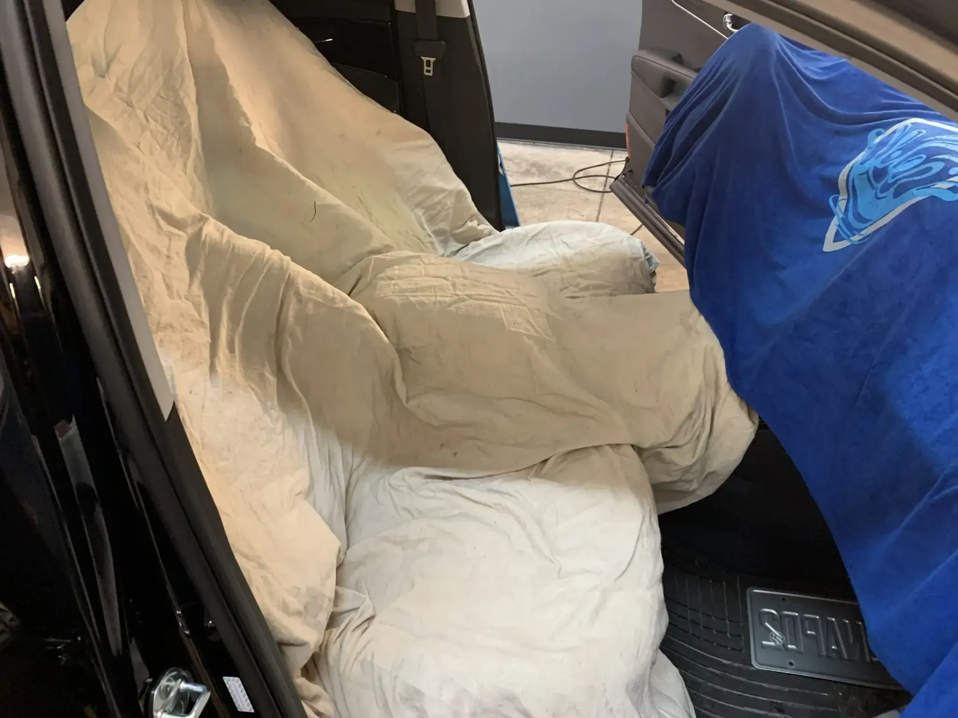 Car seat covered with beige blanket inside a vehicle, next to a blue tarp-covered seat.