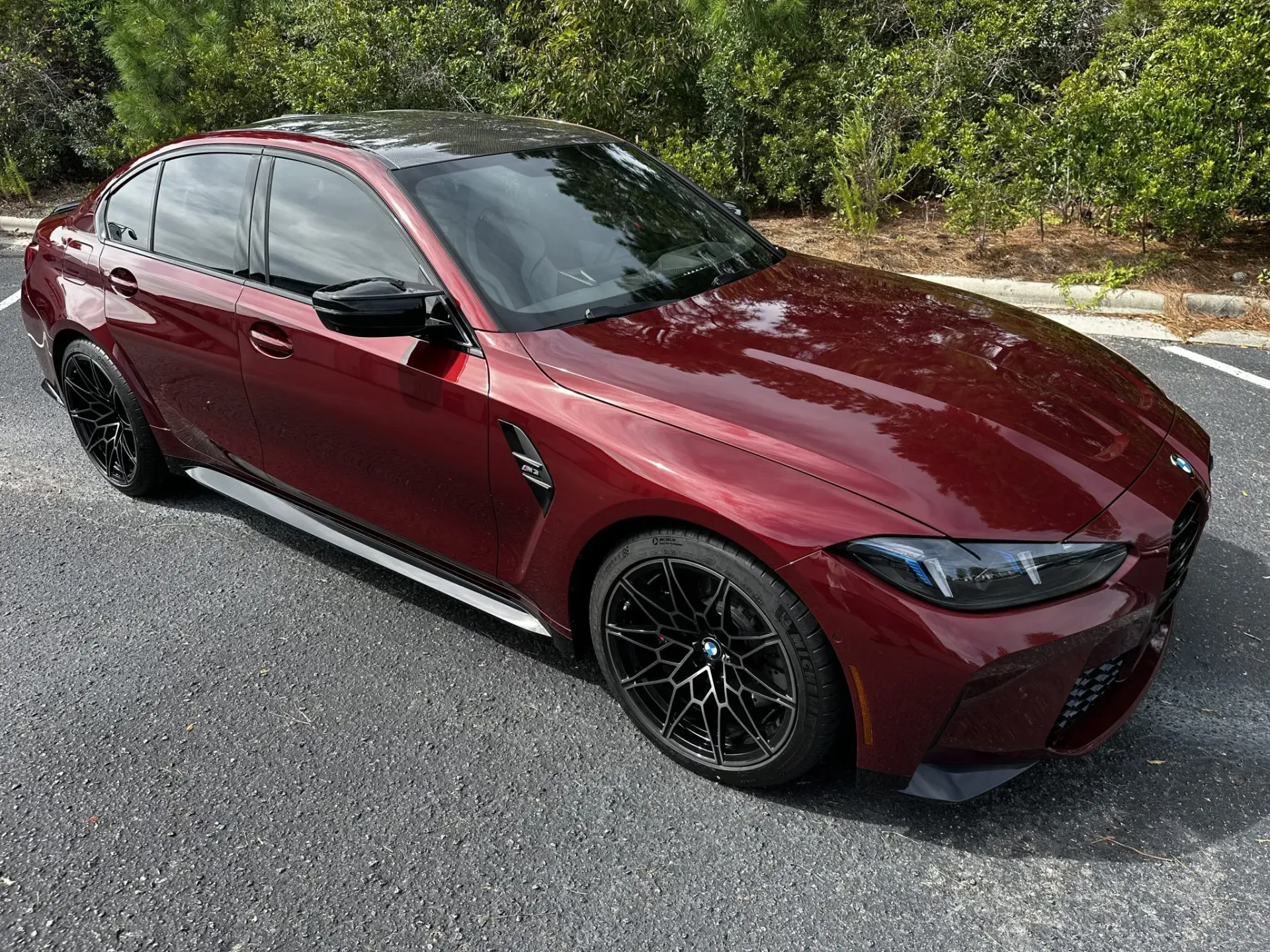 Maroon sedan parked on asphalt beside trees, viewed from the front-left side.