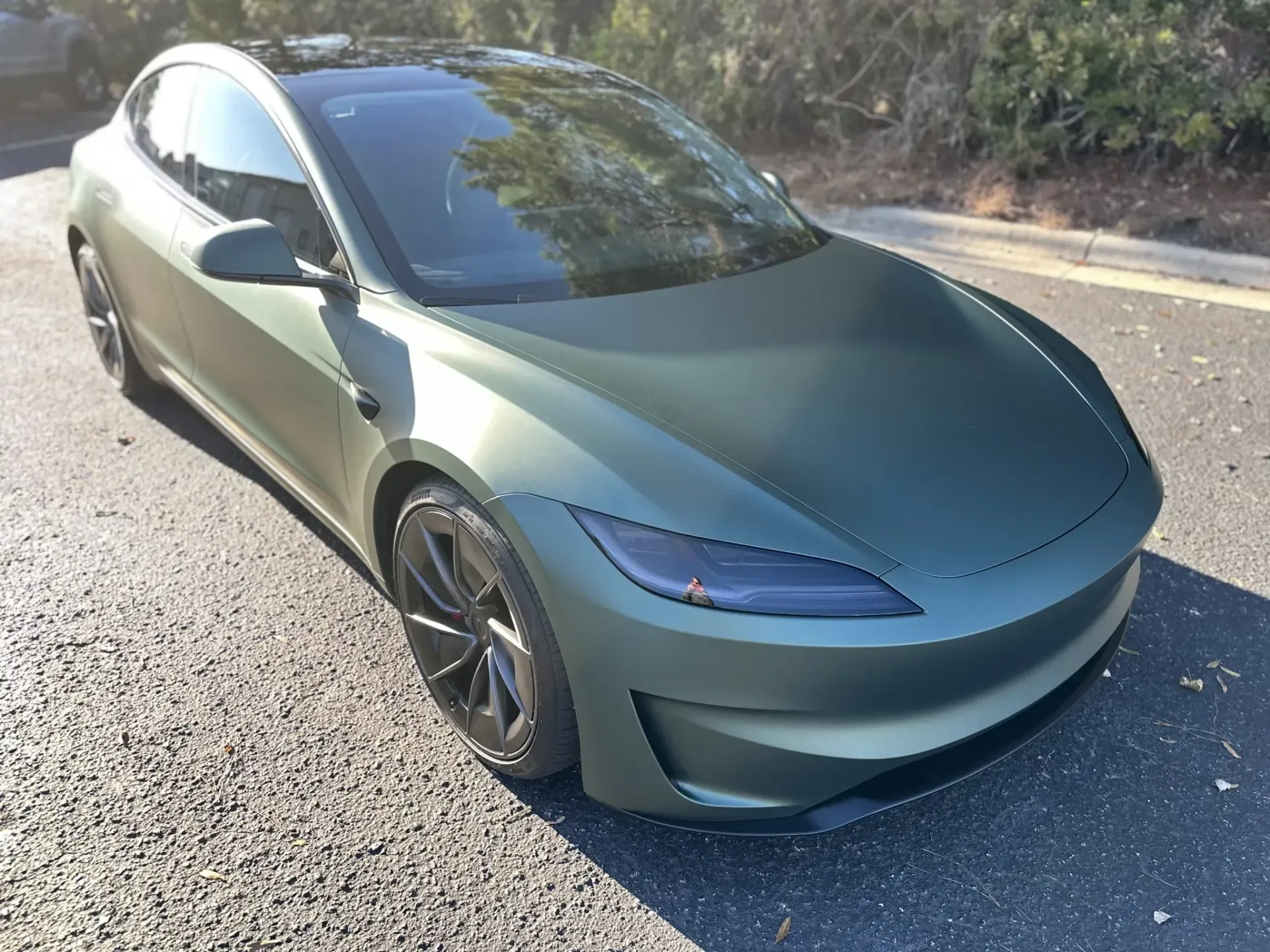 Matte green Tesla sedan parked on a gravel roadside in bright sunlight
