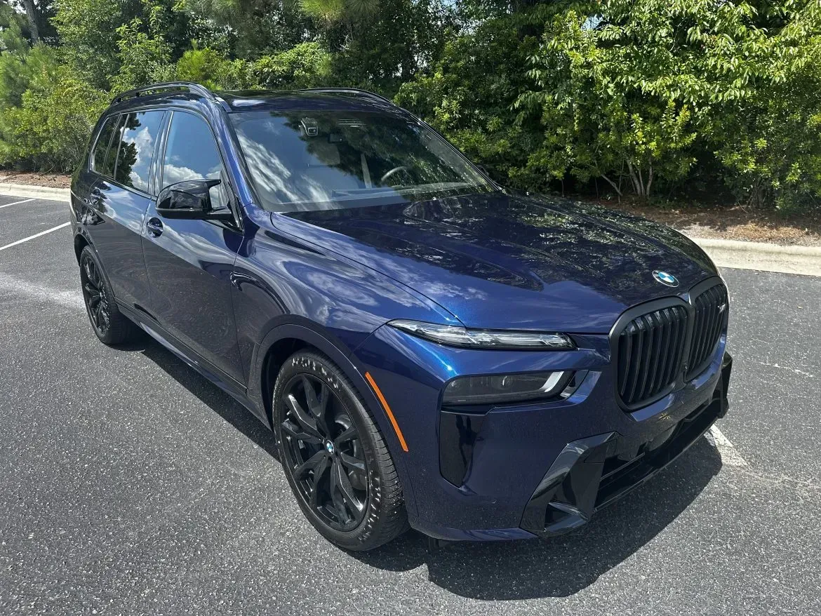 Dark blue SUV parked on asphalt beside green trees on a sunny day