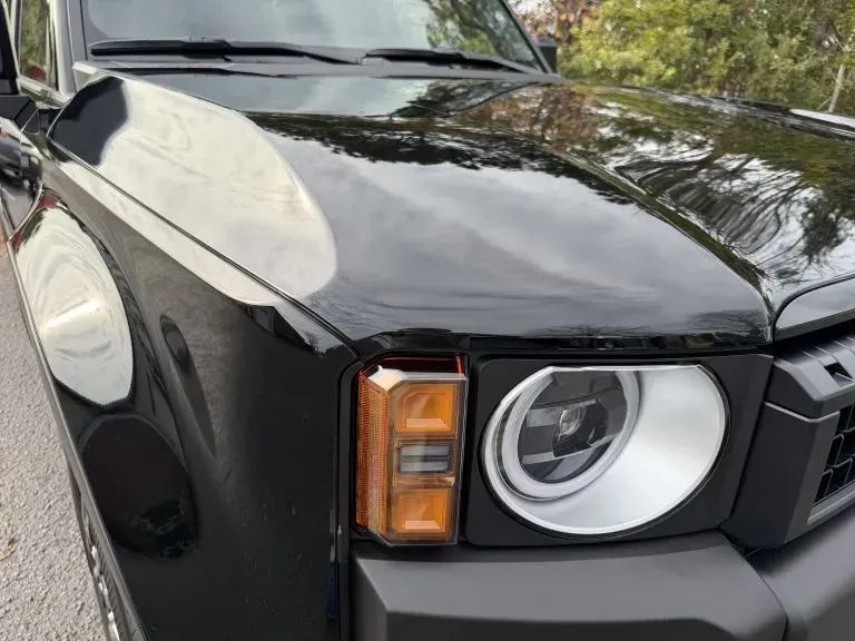 Front view of a black SUV with a round headlight and amber side marker, parked outdoors.