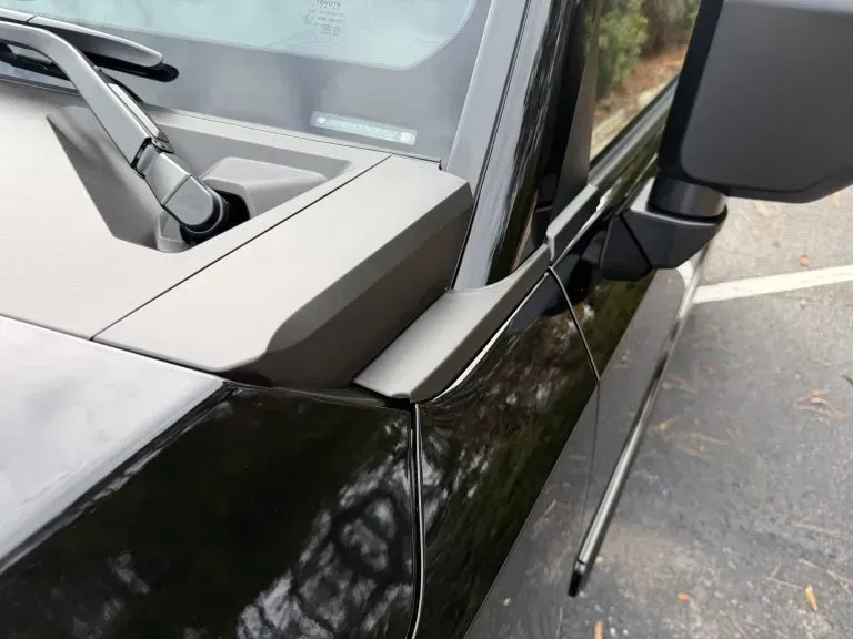 Close-up of a black car’s front passenger side, showing a broken side mirror and windshield crack