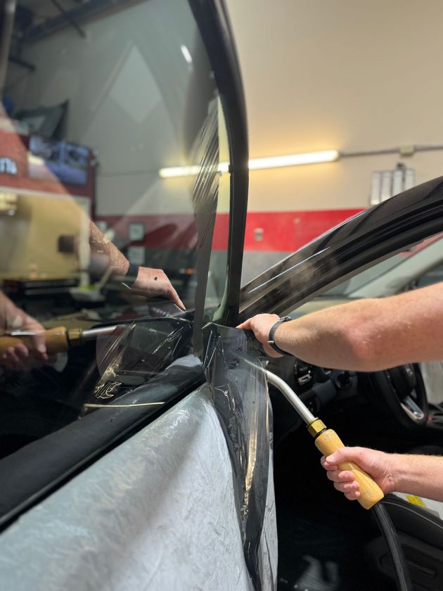 Hands repairing a car windshield with a glue gun in an auto shop