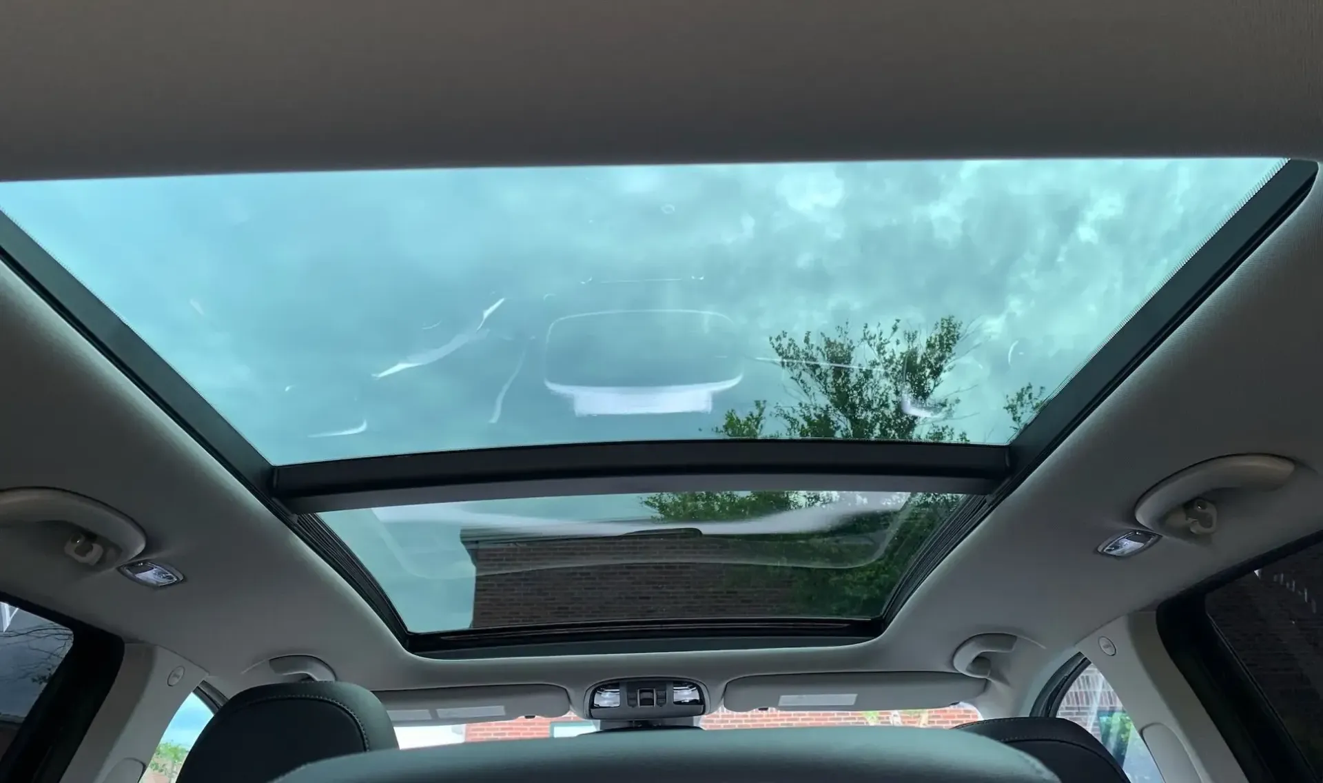 Car interior with a panoramic sunroof showing cloudy sky and trees overhead