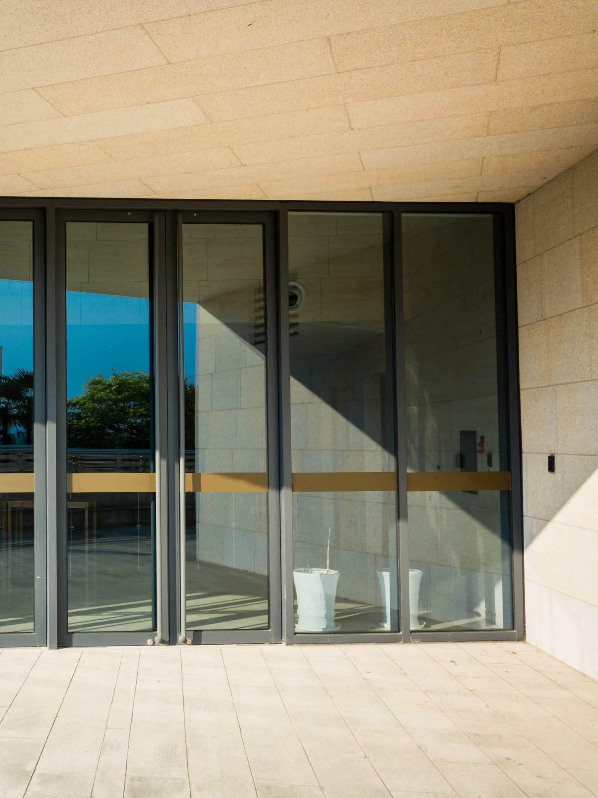 Modern building patio with floor-to-ceiling glass doors and beige stone walls, reflecting a sunny exterior