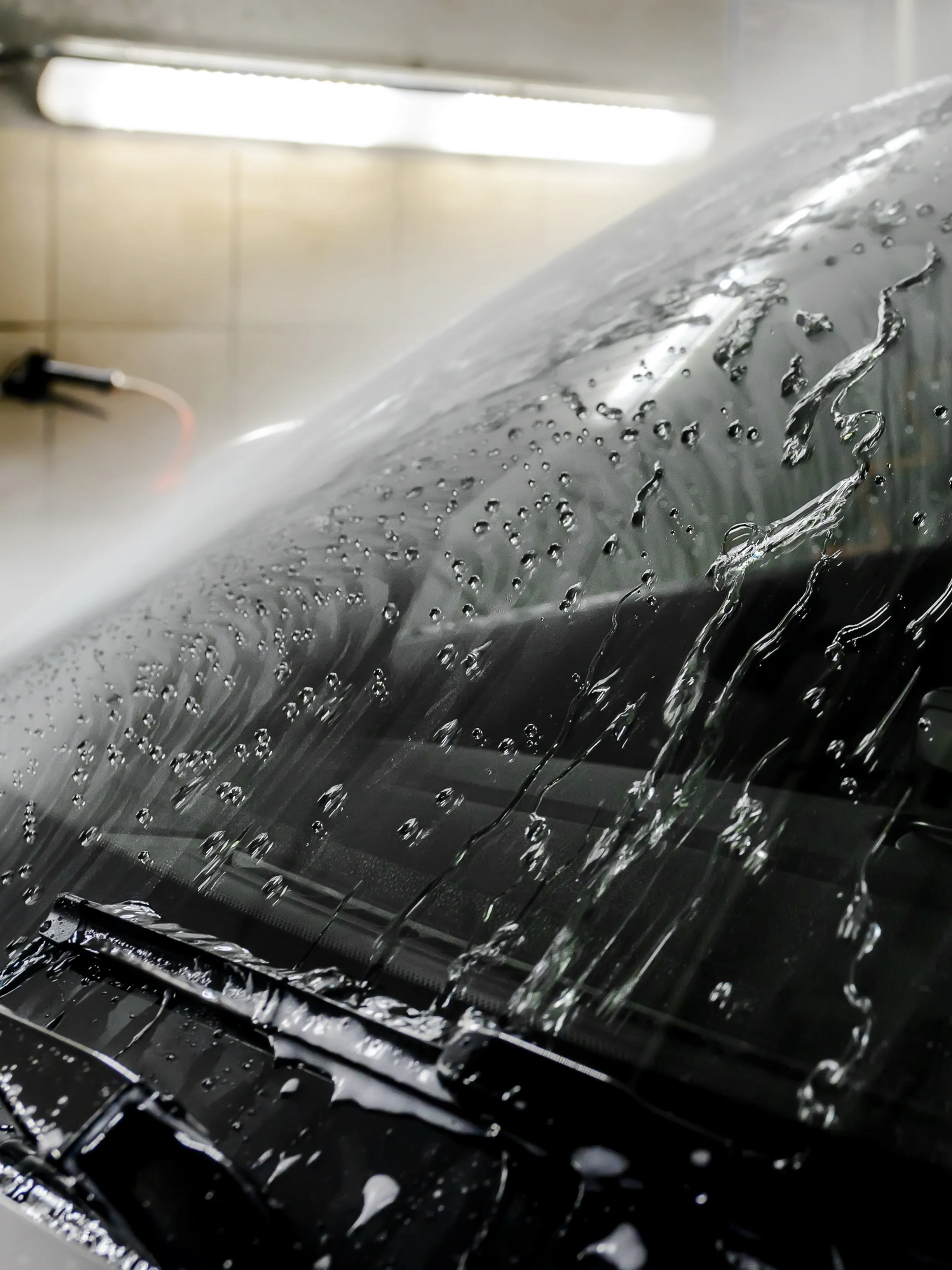 Car windshield being washed, covered in soap and water in an indoor wash bay