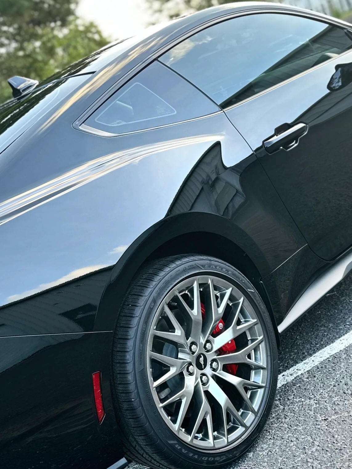 Black sports car with tinted windows and silver alloy wheel, parked on a road.