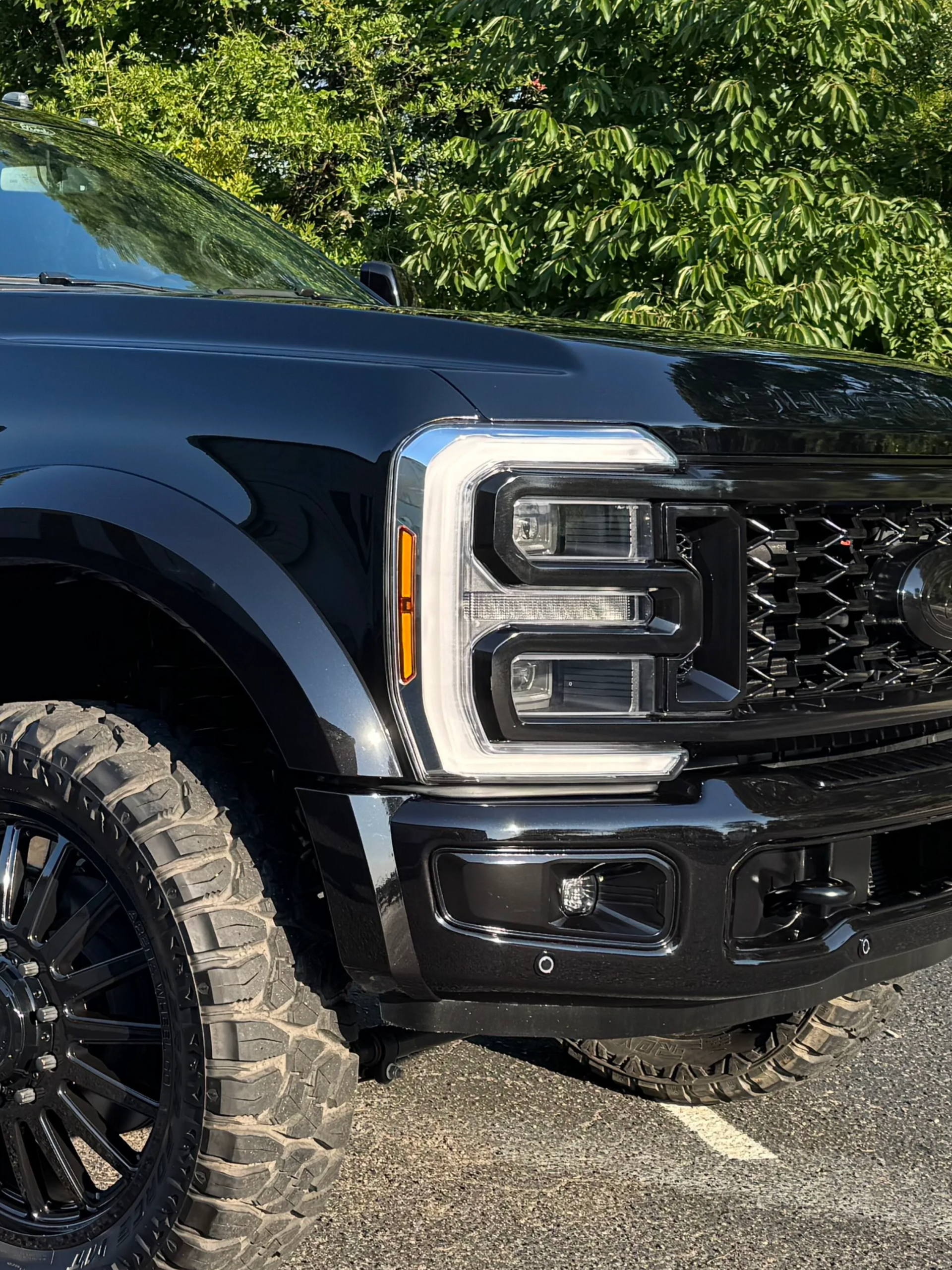 Black pickup truck front end with chrome grille parked outdoors on a paved lot near greenery