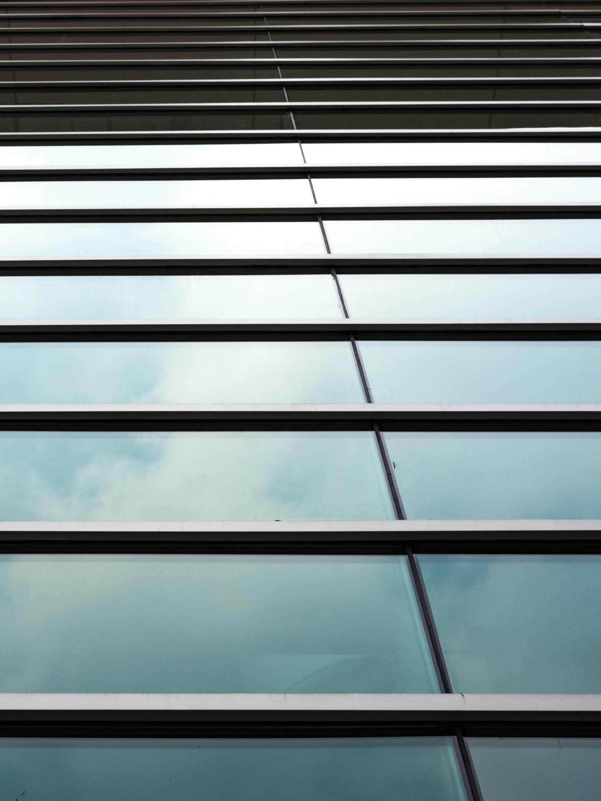 Glass building facade with horizontal blinds reflected in blue-tinted windows