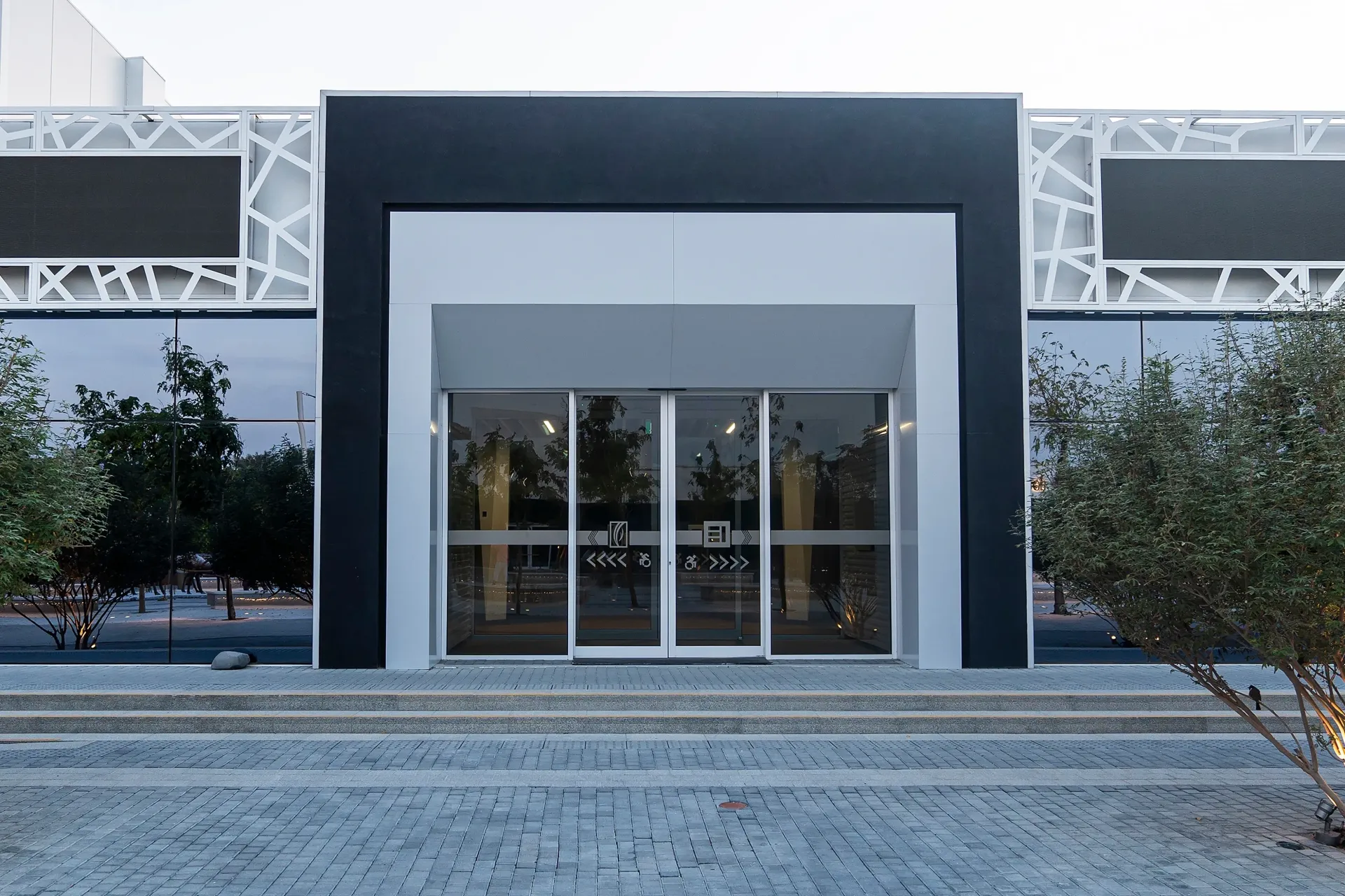 Modern building entrance with glass doors, gray facade, and trees on both sides