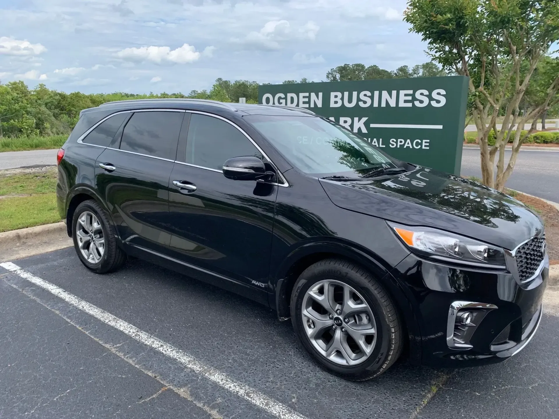 Black SUV parked in a lot beside an Ogden Business Park sign under a partly cloudy sky