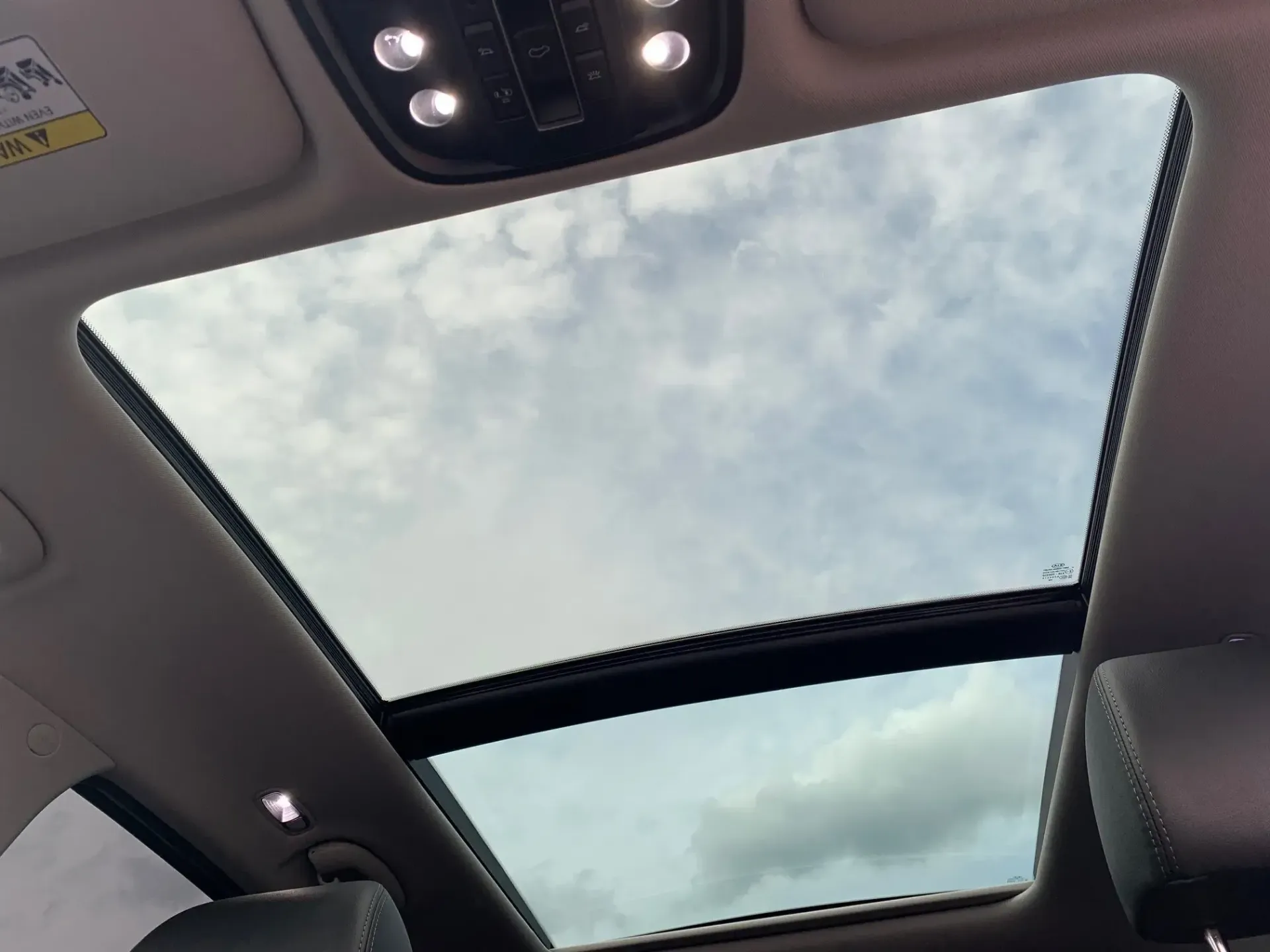 Car interior with panoramic sunroof showing cloudy sky overhead.