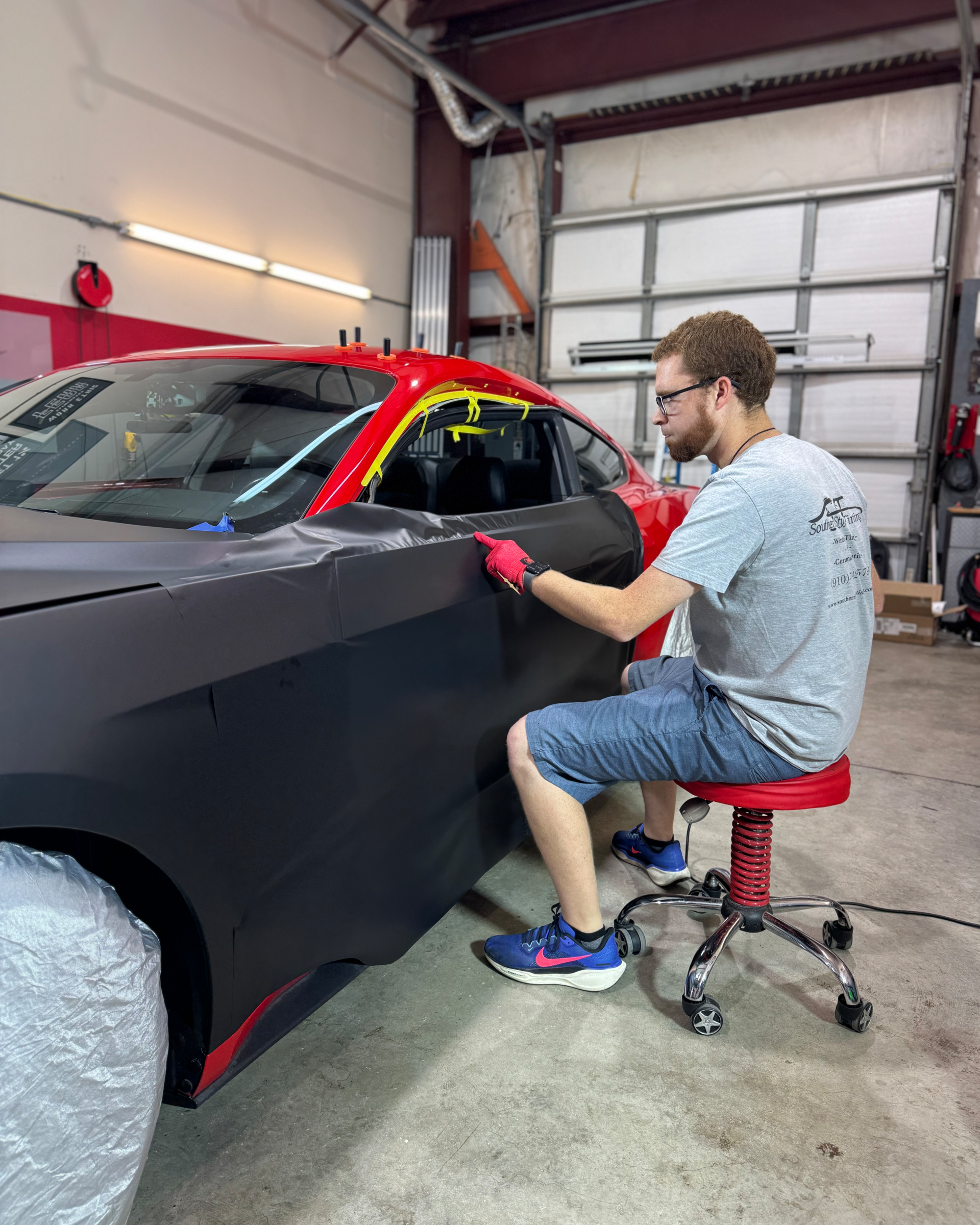 Painter applying red tape to a black car in a workshop