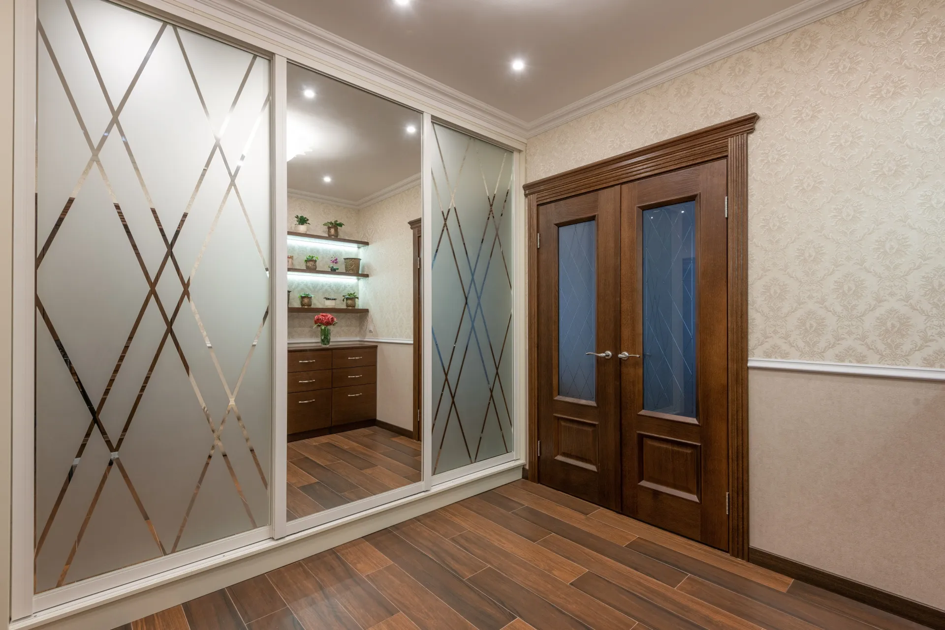 Modern room with frosted sliding closet doors, a mirrored section, wooden floor, and a double wooden door.
